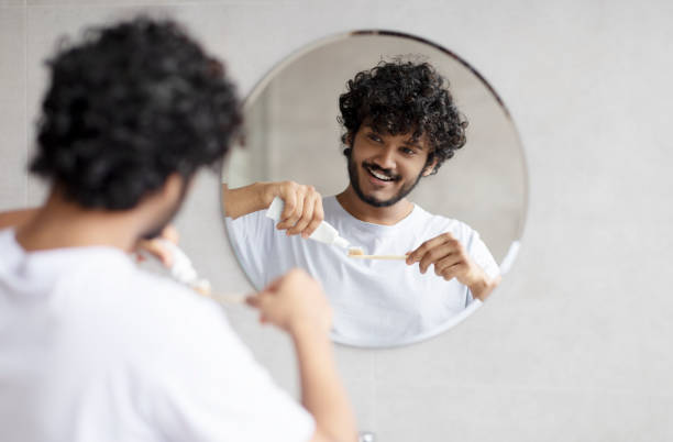 istock Indian man cleaning teeth in the morning, applying toothpaste on toothbrush, looking at mirror in bathroom, free space 1464830302