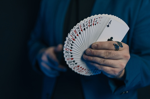 Close-up image of a young magician's hands in the dark with a fan-shaped deck of cards showing the front of the deck.
