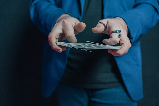 Close-up image of a young magician in the dark holding a deck of cards with both hands and intermingling them with each other.