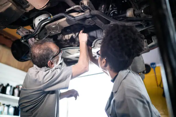 Photo of Auto mechanic man teaching his assistant on the repair shop