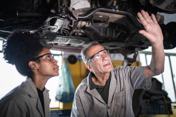 mecânico de automóveis ensinando o seu assistente na oficina - auto repair shop mechanic garage workshop - fotografias e filmes do acervo