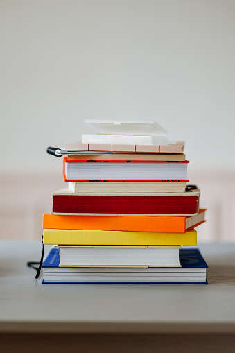 A view of a table with a stack of colourful books on it. (reading, studying, learning, education concept)