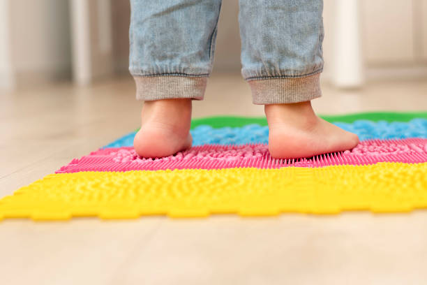 health concept. a little boy stands with bare feet on a multi-colored orthopedic massage mat. - plattfot bildbanksfoton och bilder
