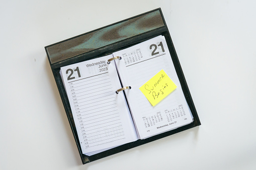 An open daily calendar with a yellow sticky note reminder of  the beginning of Summer.