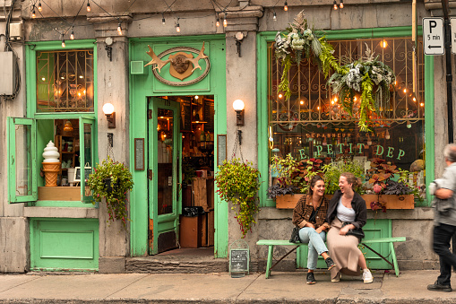 Montreal, Canada - September 25, 2021:  Two women laugh on a bench in front of a traditional cafe bistro restaurant in the Old Town Montreal, Quebec Canada