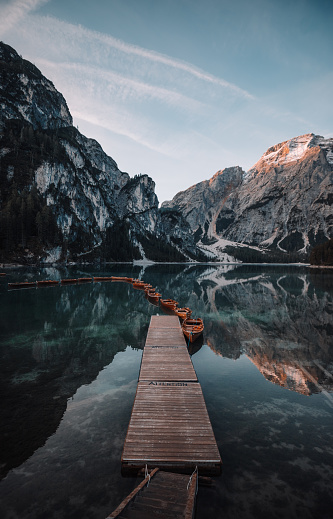 Beautiful lake in nature and summer with a wooden pier, orange boats and mountain reflection during sunrise  at a beautiful turquoise water lake Lago di Braies, Trentino Alto Adige, South Tirol, European Alps, Italia, South Europe