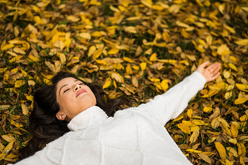 Tranquil pregnant woman laying on ground with arms outstretched on autumn day in nature.