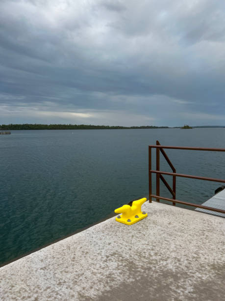 Bright Yellow Boat Cleat Overlooking Lake Superior A bright yellow boat cleat affixed to a large cement dock. Rain has just fallen. Commercial dock is set upon Lake Superior looking out over natures pristine natural beauty. Located on the northern island of Isle Royale National Park within the Upper Peninsula of Michigan. Boat or sea plane are the only modes of transportation available to reach this remote location. bollard pier water lake stock pictures, royalty-free photos & images