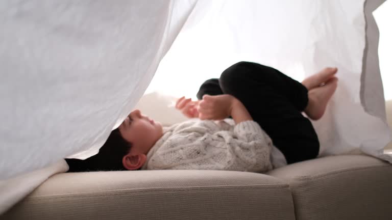 Smiling little boy hiding under sheet