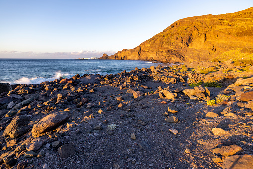 Sunset on the rocky shore with small white buildings at the end of cliff