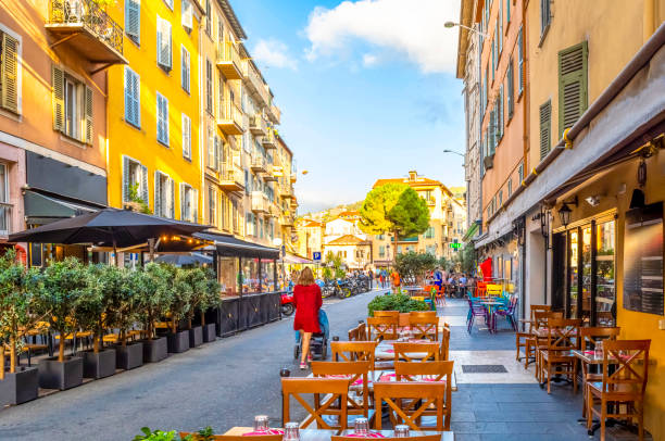 uma mulher empurra um carrinho de bebê através de um café e loja alinhada rua estreita na cidade velha vieux nice, na cidade mediterrânea de nice, frança, na riviera francesa. - city of nice fotos - fotografias e filmes do acervo