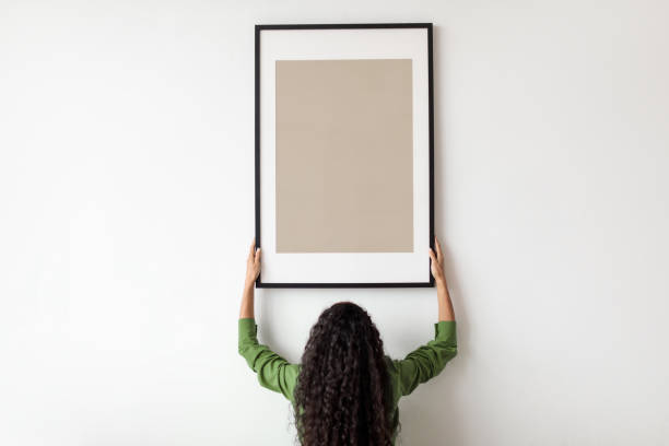 istock Unrecognizable Female Hanging Blank Poster In Frame On Wall Indoor 1464865626