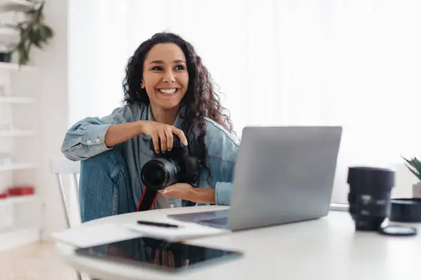 Photo of Happy Photographer Woman Holding Photocamera Using Laptop Computer Sitting Indoor