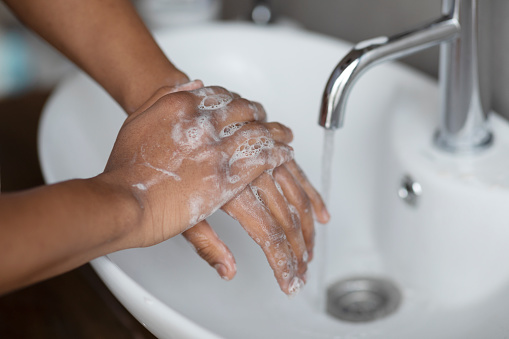 Handwashing concept. Young indian man washing hands with antibacterial soap under falling tap water in wash-basin in modern bathroom, closeup