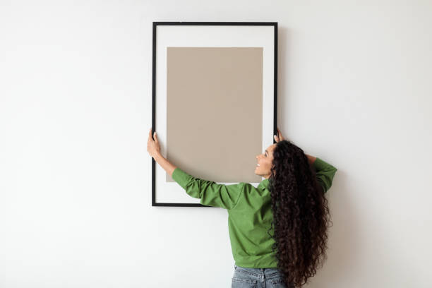 istock Woman Hanging Frame With Empty Poster On White Wall Indoors 1464866945