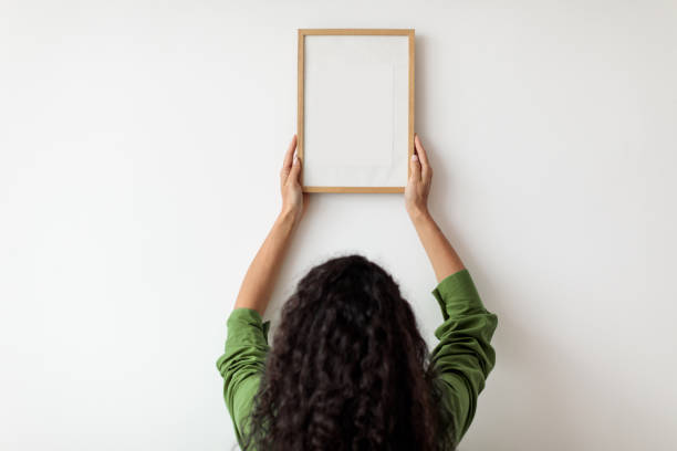 istock Back-View Of Lady Hanging Picture Frame On Wall Indoors 1464866954