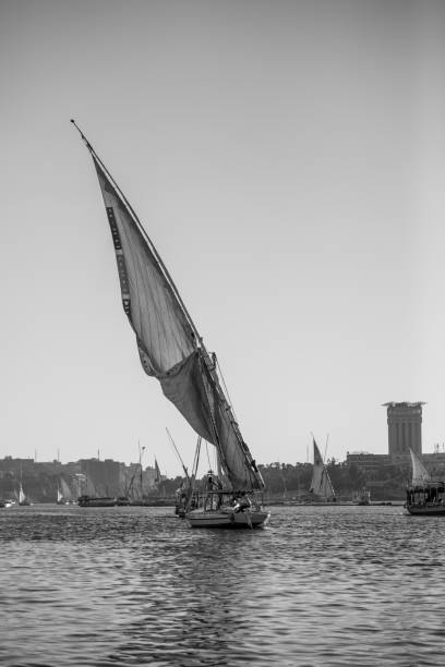 Captivating photo of a traditional Egyptian boat sailing on the Nile River during a golden sunset in Luxor, Egypt. The vivid orange sky, silhouettes of palm trees and buildings, and the glowing sun create a romantic and serene atmosphere. Perfectly capturing the magic of a Nile cruise, this image reflects Egyptian culture, scenic beauty, and the timeless charm of river life in one of the world’s most historic regions.