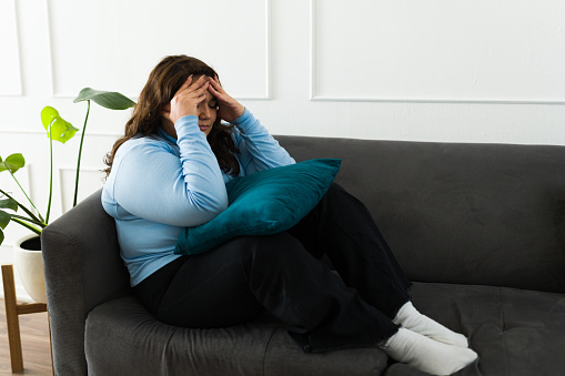 Anxious sad overweight woman feeling sad and depressed while looking lonely sitting on the sofa