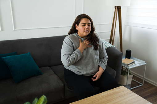 Stressed hispanic woman suffering from hyperventilation or an anxiety attack while feeling stressed at home