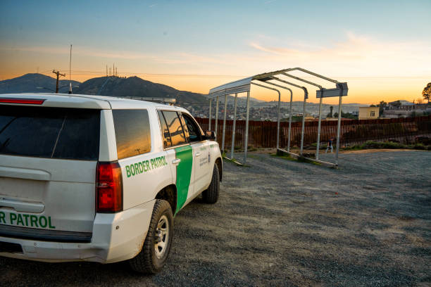 veicolo ufficiale della pattuglia di frontiera degli stati uniti parcheggiato vicino al muro della barriera di confine internazionale tra stati uniti e messico a tecate california al crepuscolo con un bel paesaggio nuvoloso - department of homeland security foto e immagini stock