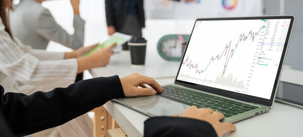 istock Businesswoman in analyze stock market data using laptop computer proficiently at the office while attending a group meeting with business team . 1464893322