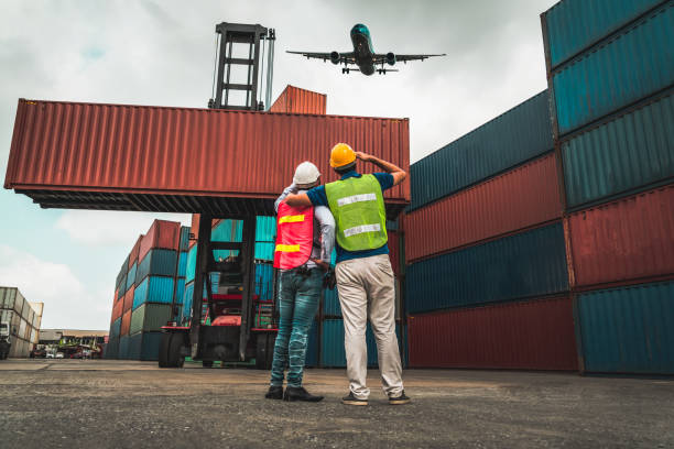 istock Industrial worker works with co-worker at overseas shipping container port . Logistics supply chain management and international goods export concept . 1464893685