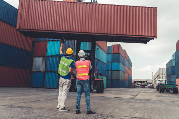 istock Industrial worker works with co-worker at overseas shipping container yard . Logistics supply chain management and international goods export concept . 1464896813