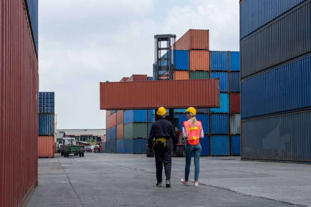 istock Industrial worker works with co-worker at overseas shipping container yard . Logistics supply chain management and international goods export concept . 1464898334