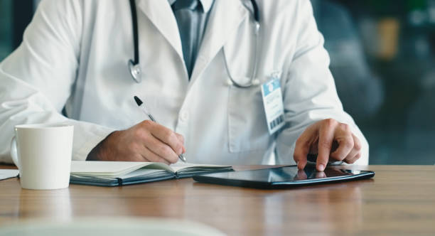 istock Doctor, hands and tablet writing in notebook for planning, schedule or notes for medical documents at office. Hand of healthcare professional in strategy, book or prescription in Telehealth on desk 1464901803