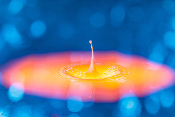 The drop falls into a dense liquid with a blue-yellow background. Abstract colorful background