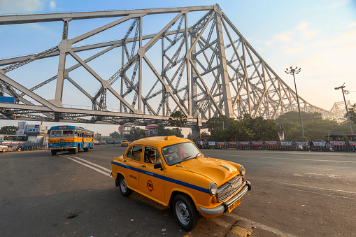Taxi parked on city road near Howrah bridge at sunrise with view of early morning traffic at Kolkata, India shot on November 18, 2022