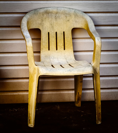 An old yellow plastic chair stands near a wall in the backyard.