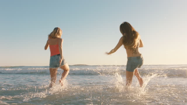 girl friends running on beach into sea having fun splashing in water teenage girls enjoying warm summer day on vacation