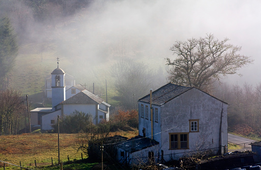 Small village  in fog, rural area, houses, slate rooftops,  church bell tower, view from above. Lugo province, Fonsagrada, Galicia, Spain.