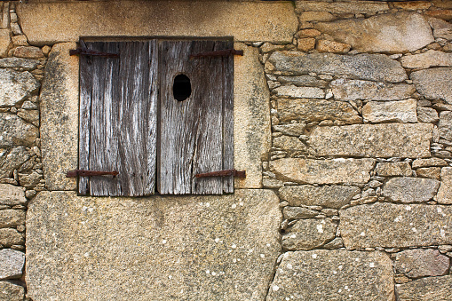 Part of old weathered stone facade and closed window. Ribeira Sacra, Galicia, Spain.