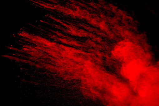 Red powder explosion cloud on black background. Freeze motion of red color dust  particles splashing.