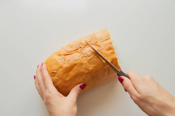 istock female hand cuts a piece of bread with a knife on a white table in the kitchen 1464932895
