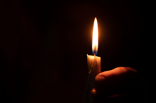 candle flame illuminates a female hand in a dark room