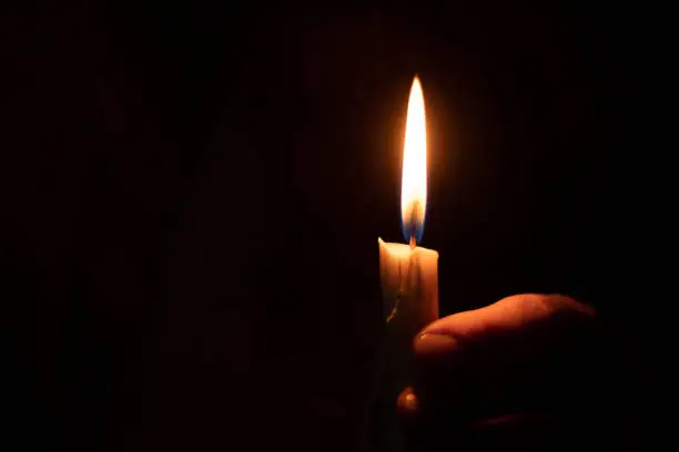 Photo of candle flame illuminates a female hand in a dark room