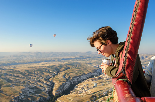 Young woman in hot air balloon basket, looking at balloons and beautiful landscape of Goreme, travel vacation in Cappadocia, Turkey