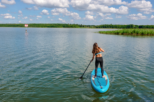 Girl paddling on SUP board on beautiful lake, standing up paddle boarding adventure in Germany lake district Mecklenburg