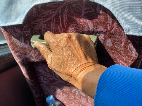 Old man's dry and wrinkled hand clings to the pull knob of the bus backseat. pov