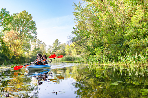 Heterosexual couple enjoying kayaking on river. Cheerful man and woman are paddling kayak together. They are on summer vacation.
