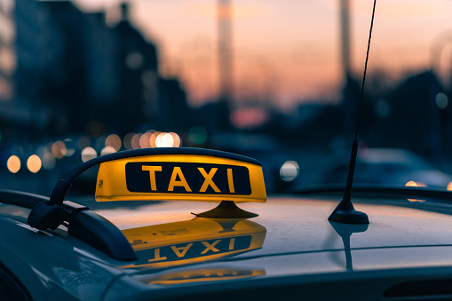 A close-up shot of a taxi sign in the warm colours of sunset with bokeh lights in the background. Urban transportation.