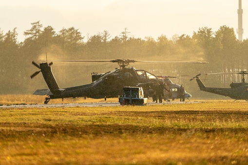 An AH-64 military attack helicopter departing from a grass field.