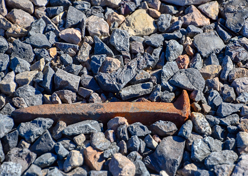A weathered rusty railroad spike laying among gravel rocks
