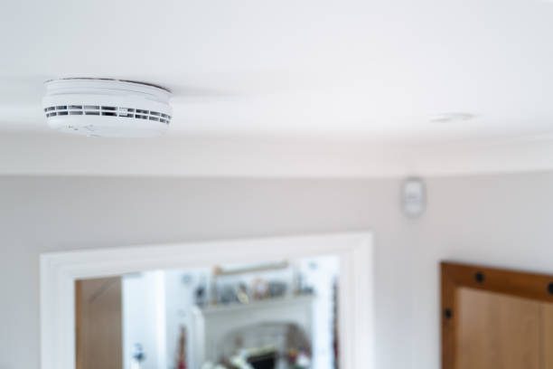 Shallow focus of a hard wired smoke detector seen in the downstairs hall, fixed to the ceiling. stock photo