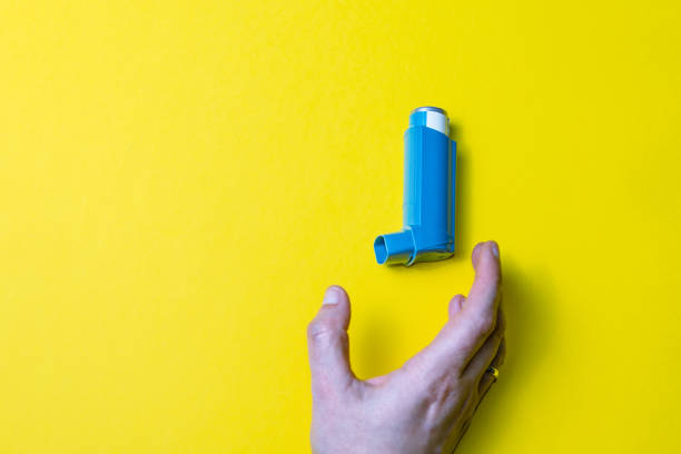 istock Hand holding an asthma inhaler on  yellow background 1464956995