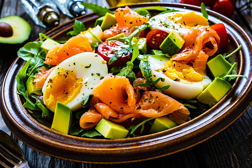 Smoked salmon with boiled egg, avocado and leafy vegetables on wooden table