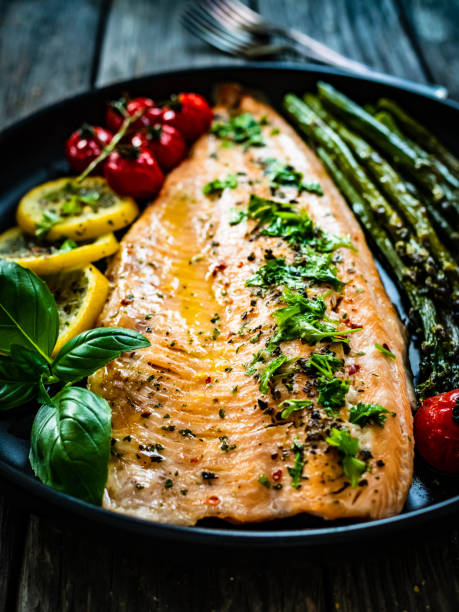 istock Fried salmon fillet, asparagus and fried tomatoes on wooden background 1464961069